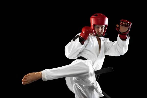 Beyaz dobok giymiş erkek tekvando dövüşçüsü, kask ve eldiven eğitimi karanlık arka planda izole edilmiş. Spor anlayışı, antrenman, rekabet, reklam — Stok fotoğraf