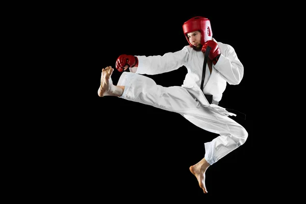 Combatiente taekwondo masculino en dobok blanco, casco y guantes entrenando aislado sobre fondo oscuro. Concepto de deporte, entrenamiento, competición, anuncio — Foto de Stock