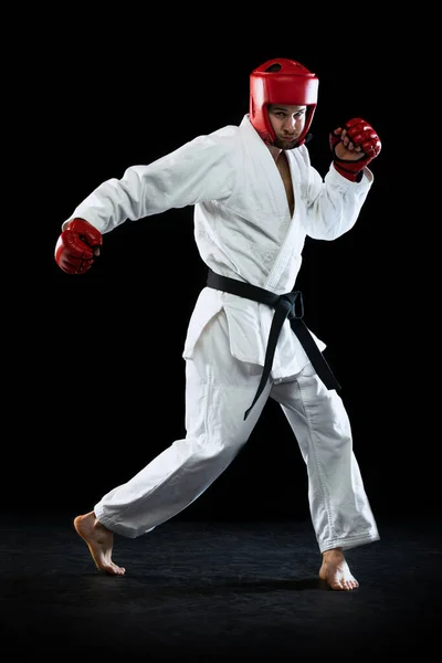 Caça taekwondo macho em dobok branco, capacete e luvas de treinamento isolado sobre fundo escuro. Conceito de esporte, treino, competição, anúncio — Fotografia de Stock