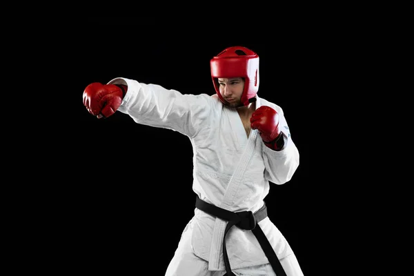 Beyaz dobok giymiş erkek tekvando dövüşçüsü, kask ve eldiven eğitimi karanlık arka planda izole edilmiş. Spor anlayışı, antrenman, rekabet, reklam — Stok fotoğraf