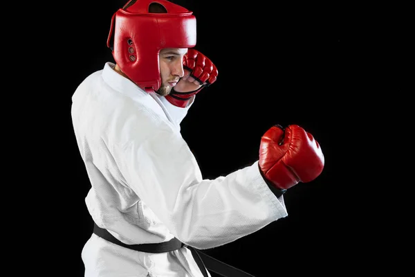 Male taekwondo fighter in white dobok, helmet and gloves training isolated over dark background. Concept of sport, workout, competition, ad — 스톡 사진