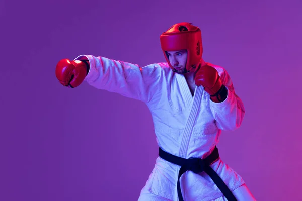 Stúdió lövés férfi taekwondo harcos sport egyenruhában akcióban elszigetelt lila háttér neon fény. Fogalom a sport, edzés, verseny, reklám — Stock Fotó