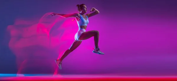 Flyer with professional female athlete, runner training isolated on blue studio background in mixed pink neon light. Sport, motion and action concept. — Stock fotografie