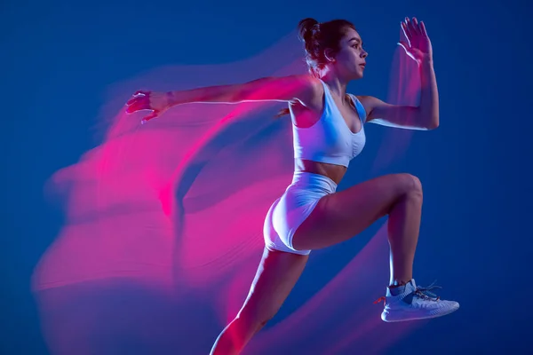 Profile view of female athlete, runner training isolated on blue studio background in mixed pink neon light. Healthy lifestyle, sport, motion and action concept. —  Fotos de Stock