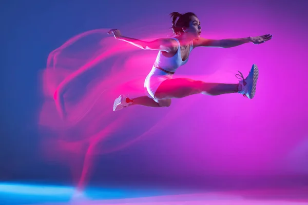 Профессиональная спортсменка, бегун тренировки изолированы на синем фоне студии в смешанном розовом неоновом свете. Здоровый образ жизни, спорт, движение и концепция действий. — стоковое фото