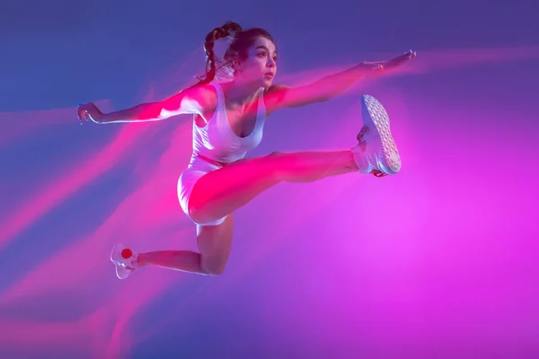 Профессиональная спортсменка, бегун тренировки изолированы на синем фоне студии в смешанном розовом неоновом свете. Здоровый образ жизни, спорт, движение и концепция действий. — стоковое фото