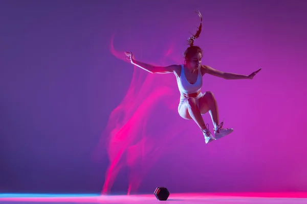 Jovem, atleta treinando isolado em fundo estúdio azul em luz de néon rosa mista. Estilo de vida saudável, esporte, movimento e conceito de ação. — Fotografia de Stock