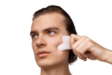 Mükemmel pürüzsüz ciltli, beyaz stüdyo arka planına izole edilmiş yüz masajları yapan çekici bir genç. Kozmetik, sağlık, cilt bakımı, güzellik