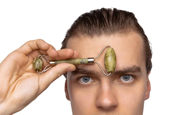 Young attractive man with perfect smooth skin, applying face massagers isolated over white studio background. Cosmetics, health care, skin care, beauty — Stockfoto