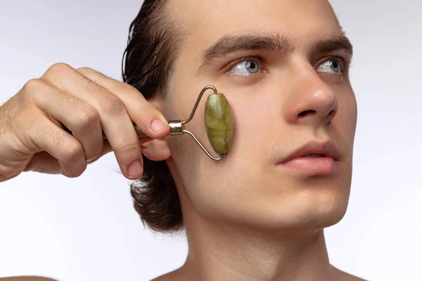 Young attractive man with perfect smooth skin, applying face massagers isolated over white studio background. Cosmetics, health care, skin care, beauty — 스톡 사진