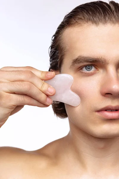 Young attractive man with perfect smooth skin, applying face massagers isolated over white studio background. Cosmetics, health care, skin care, beauty — Stockfoto