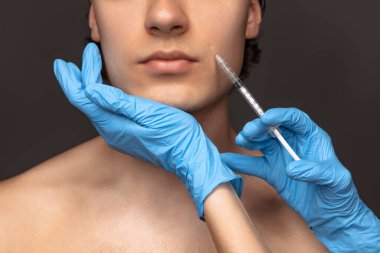 Siyah arka planda, mavi eldivenli genç adam ve kadın ellerinin yakın plan fotoğrafı. Kozmetik, ameliyat prosedürleri. Yaşlanma karşıtı kavram.