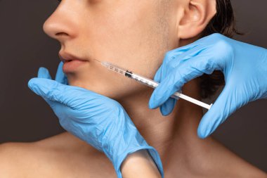 Siyah arka planda, mavi eldivenli genç adam ve kadın ellerinin yakın plan fotoğrafı. Kozmetik, ameliyat prosedürleri. Yaşlanma karşıtı kavram.