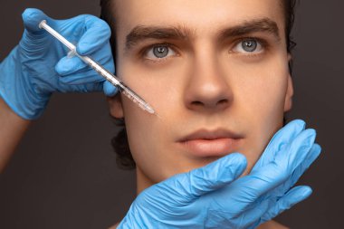 Siyah arka planda, mavi eldivenli genç adam ve kadın ellerinin yakın plan fotoğrafı. Kozmetik, ameliyat prosedürleri. Yaşlanma karşıtı kavram.