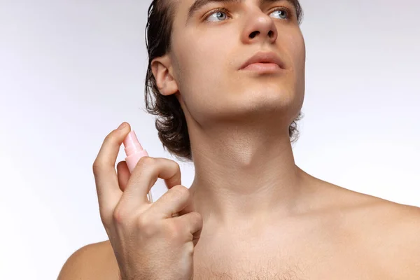 Portrait of young attractive man with perfect smooth skin, applying face cream isolated over white studio background. Cosmetics, health care, skin care, beauty — Stockfoto