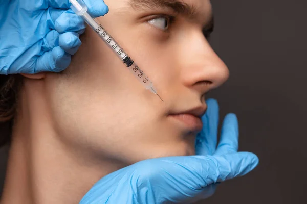 暗い背景に隔離された注射器と青手袋で若い男と女の手のクローズアップ顔。化粧品、充填手術手順。アンチエイジングの概念. — ストック写真