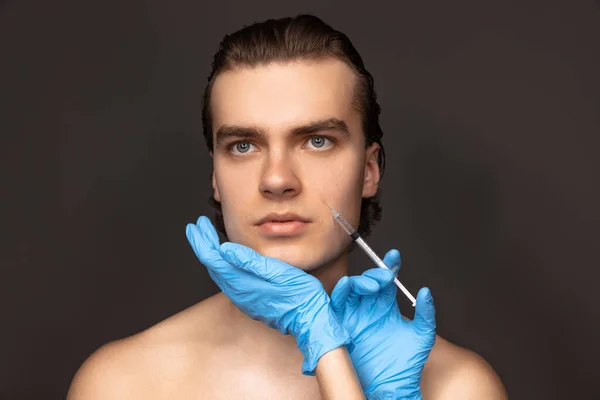 暗い背景に隔離された注射器と青手袋で若い男と女の手のクローズアップ顔。化粧品、充填手術手順。アンチエイジングの概念. — ストック写真