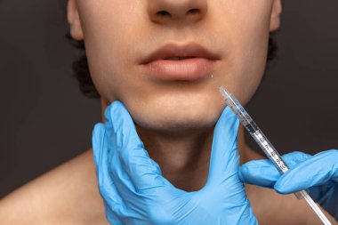 Siyah arka planda, mavi eldivenli genç adam ve kadın ellerinin yakın plan fotoğrafı. Kozmetik, ameliyat prosedürleri. Yaşlanma karşıtı kavram.