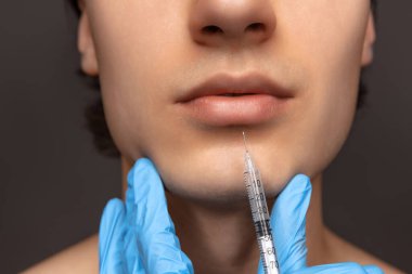 Siyah arka planda, mavi eldivenli genç adam ve kadın ellerinin yakın plan fotoğrafı. Kozmetik, ameliyat prosedürleri. Yaşlanma karşıtı kavram.