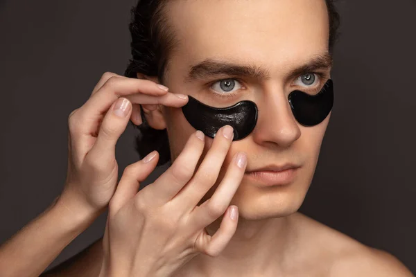 Young adorable man with well-kept skin using patches under eyes isolated over grey background. Fashion, cosmetics, health care, skin care, beauty — ストック写真
