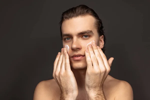 Facial skin care for man. Young happy man with perfect well-kept skin using face cream isolated over grey background. Cosmetics, health care, skin care, beauty — 스톡 사진