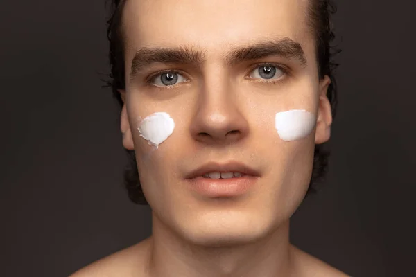 Facial skin care for man. Young happy man with perfect well-kept skin using face cream isolated over grey background. Cosmetics, health care, skin care, beauty — Stock Fotó