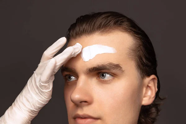 Moisturizing face mask. One man with perfect well-kept skin using face cream mask isolated over grey background. Cosmetics, health care, skin care, beauty — Stockfoto