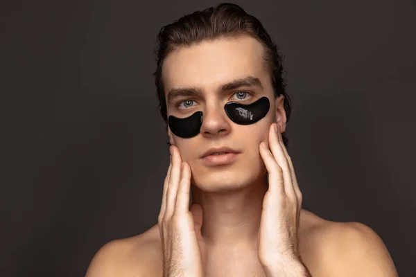 Young adorable man with well-kept skin using patches under eyes isolated over grey background. Fashion, cosmetics, health care, skin care, beauty — 스톡 사진