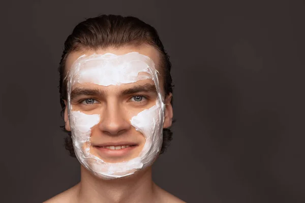 保湿フェイスマスクです。灰色の背景の上に隔離された顔のクリームマスクを使用して完全によく保たれた肌を持つ1人の男。化粧品、健康管理、スキンケア、美しさ — ストック写真