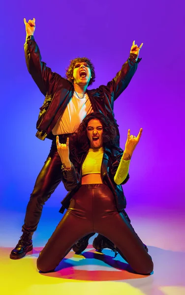 Rock music fans. Excited young man and girl in black leather outfits gesturing, shouting and dancing on blue- yellow background in neon light — Foto Stock