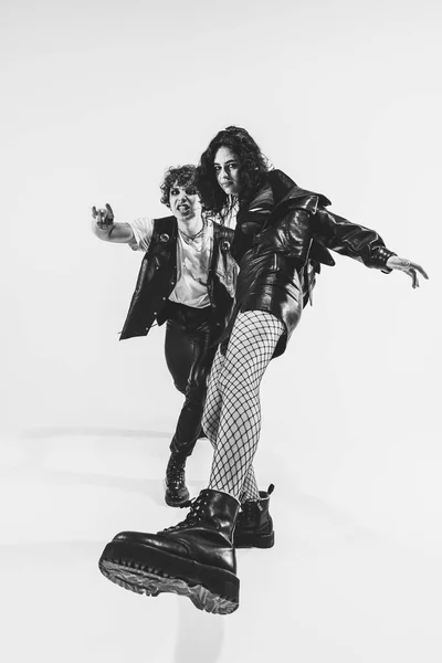 Wide angle view. Monochrome portrait of crazy musicians, young boy and girl wearing black leather outfits moving on white studio background. Music, youth — Foto Stock