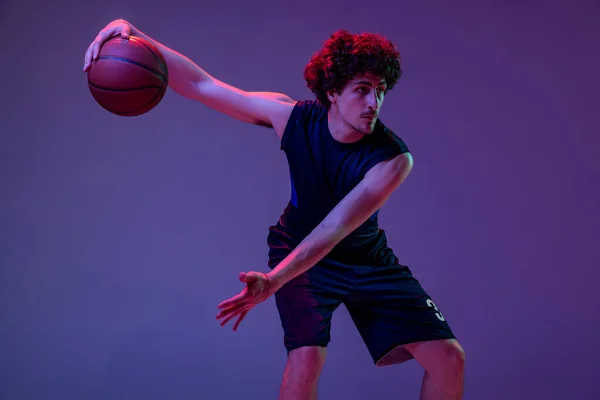 Динамічний портрет професійного баскетболіста, який стрибає з м'ячем ізольовано на фіолетовому фоні в неоні. Концепція спорту, мистецтва, створення, конкуренції . — стокове фото