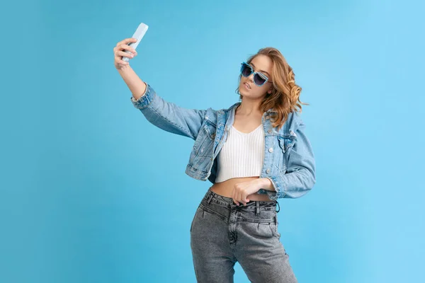 Young beautiful girl in casual style outfit using phone isolated on blue background. Concept of beauty, art, fashion, youth, fall collection — Fotografia de Stock