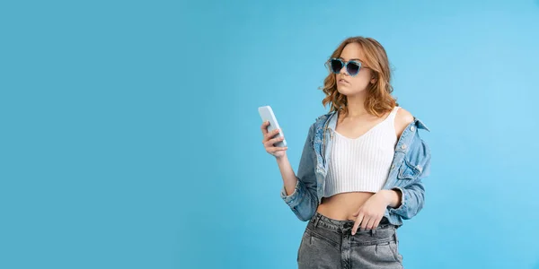 Young beautiful girl in casual style outfit using phone isolated on blue background. Concept of beauty, art, fashion, youth, fall collection