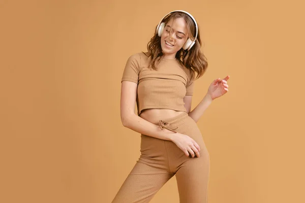 Glad flicka, student lyssnar på musik och dans isolerad över brun färg bakgrund. Begreppet skönhet, konst, mode, ungdom, monokrom — Stockfoto
