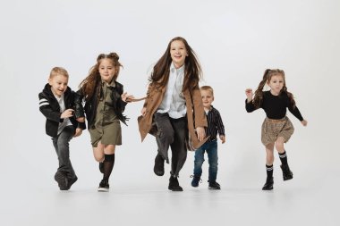 Mutlu okul ve anaokulu çocukları, koşan kızlar ve oğlanlar, gri stüdyoda izole bir şekilde atlıyorlar. Güzellik, çocuk modası, eğitim, mutlu çocukluk kavramı.