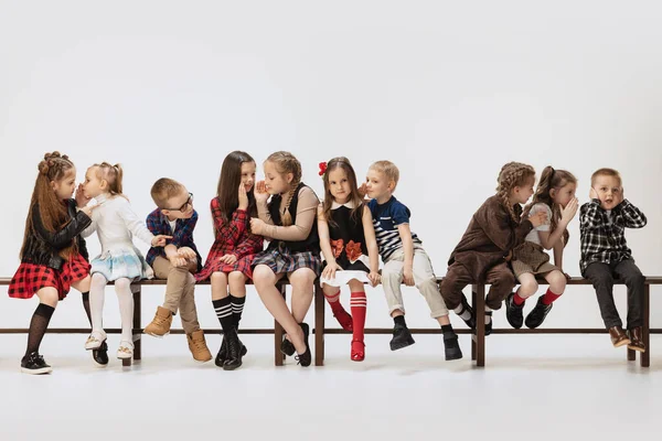 Cute, funny school and preschool age children, girls and boys sitting on banch isolated on grey studio background. Beauty, kids fashion, education, happy childhood concept. — Stockfoto