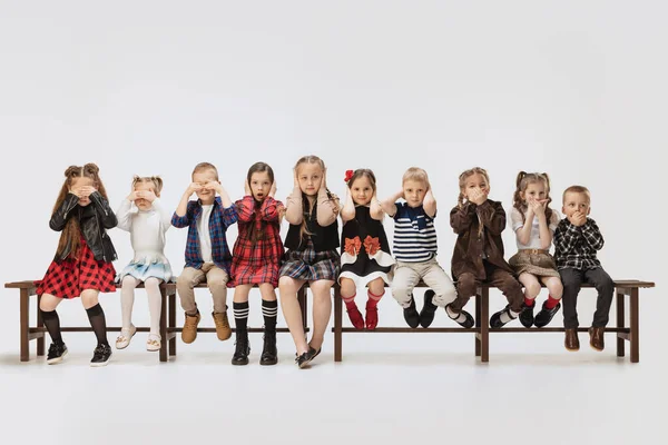 Petites filles et garçons, enfants drôles assis sur un banc isolé sur fond de studio gris. Beauté, mode enfant, éducation, concept d'enfance heureuse. — Photo