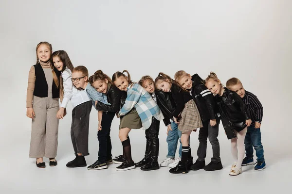 Grupo de niños lindos felices, niñas y niños con trajes modernos de pie aislado en el fondo gris del estudio. Belleza, moda infantil, educación, concepto de infancia feliz. — Foto de Stock
