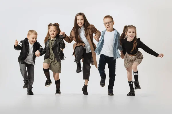 Happy school and preschool age children, girls and boys running, jumping isolated on grey studio background. Beauty, kids fashion, education, happy childhood concept. — Zdjęcie stockowe