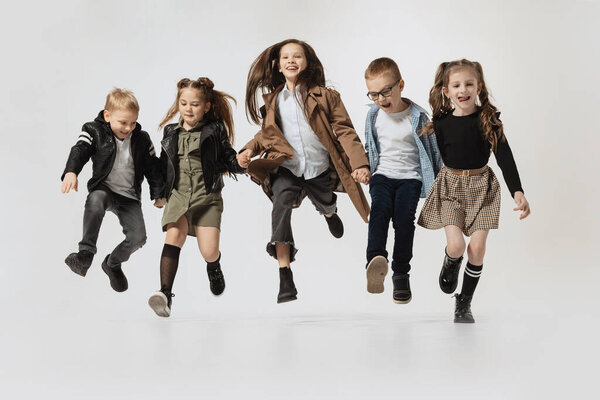 Emotional school and preschool age children, girls and boys running, jumping isolated on grey studio background. Beauty, kids fashion, education, happy childhood concept.