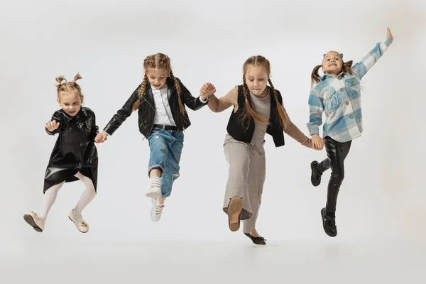 Happy school and preschool age children, beautiful girls jumping isolated on grey studio background. Beauty, kids fashion, education, happy childhood concept.