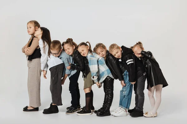 Grupo de niños lindos felices, niñas y niños con trajes modernos de pie aislado en el fondo gris del estudio. Belleza, moda infantil, educación, concepto de infancia feliz. — Foto de Stock