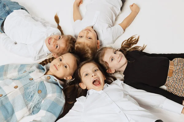 Luftaufnahme von glücklich lächelnden Schulkindern, die im Kreis liegen und in die Kamera schauen. Schönheit, Kindermode, Bildung, Konzept einer glücklichen Kindheit. — Stockfoto