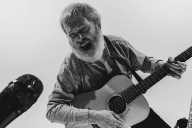 Yaşlı bir adamın siyah beyaz portresi. Müzik stüdyosunun içinde gitar çalan rock müzisyeni. Prova temeli: Sanat, müzik, tarz, eski nesil, klasik