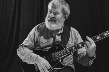 Yaşlı bir adamın siyah beyaz portresi. Müzik stüdyosunun içinde gitar çalan rock müzisyeni. Prova temeli: Sanat, müzik, tarz, eski nesil, klasik