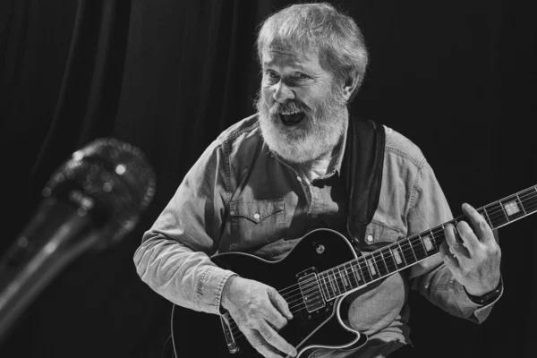 Black and white portrait of stylish old man, rock musician playing guitar at music studio interior. Rehearsal base Concept of art, music, style, older generation, vintage — 스톡 사진