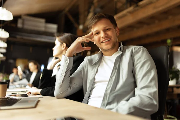 Desarrollador senior. Feliz hombre mirando a la cámara y oliendo. Trabaje en la oficina moderna del estilo del loft usando dispositivos y gadgets durante el procesamiento del trabajo. — Foto de Stock