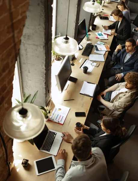 在现代商业公司的工作流程。年轻的男人和女人和同事讨论着什么，坐在办公室桌旁。团队、工作、职业的概念 — 图库照片