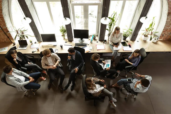 在现代商业公司的工作流程。年轻的男人和女人和同事讨论着什么，坐在办公室桌旁。团队、工作、职业的概念 — 图库照片